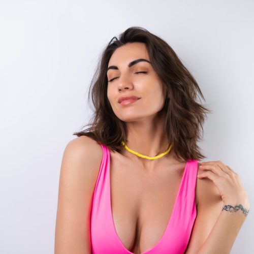 Summer portrait of a young woman in a pink swimsuit, bright yellow beach necklace